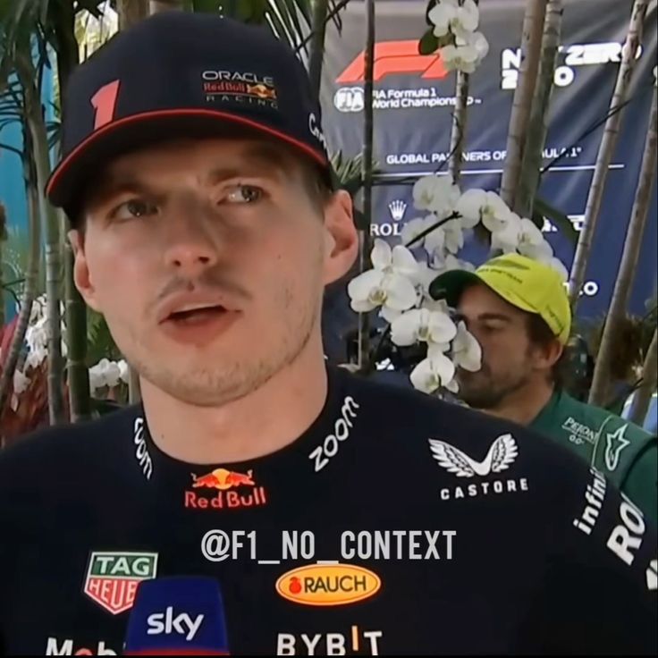 a man wearing a red bull shirt and hat in front of some palm trees with other people behind him