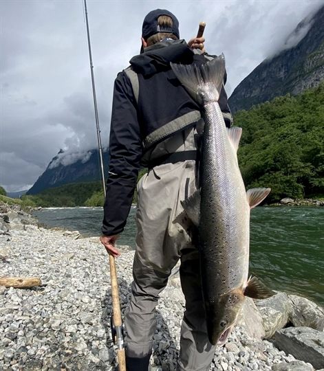 a man holding a large fish while standing on rocks