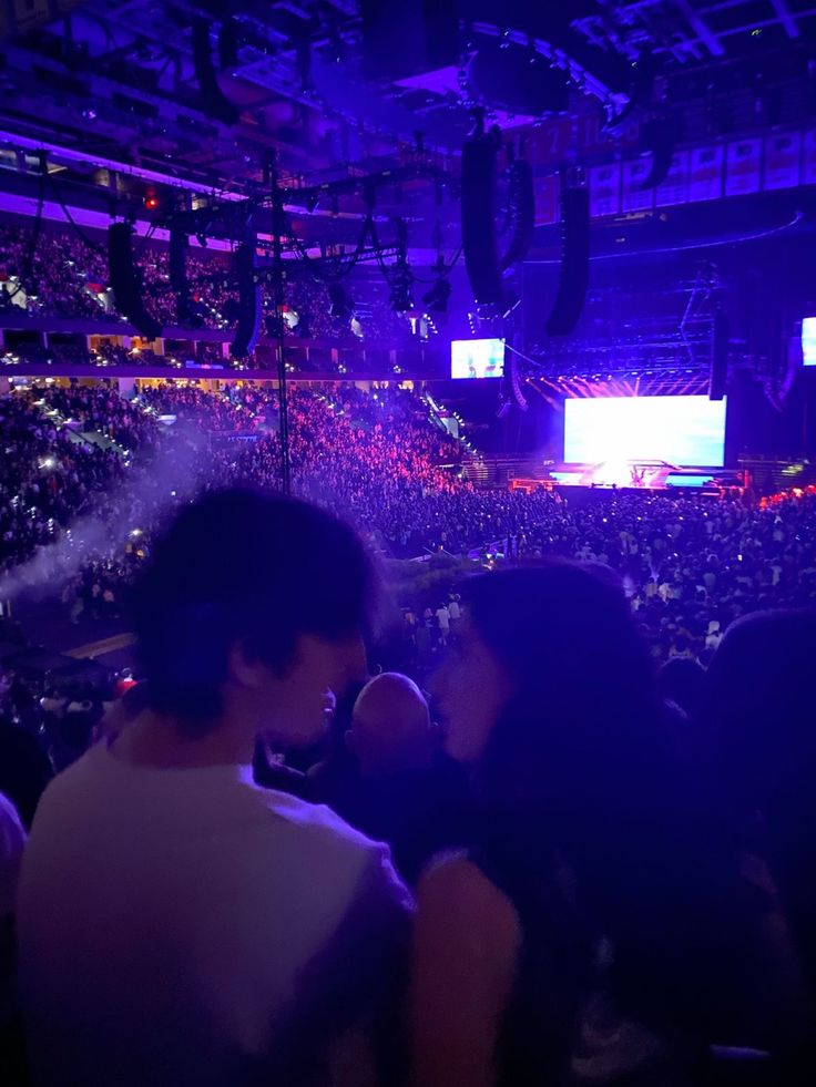 two people sitting in front of an audience at a concert with purple lighting on the stage