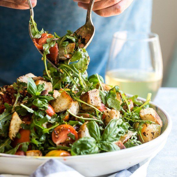 a person holding a spoon over a salad in a white bowl on top of a table