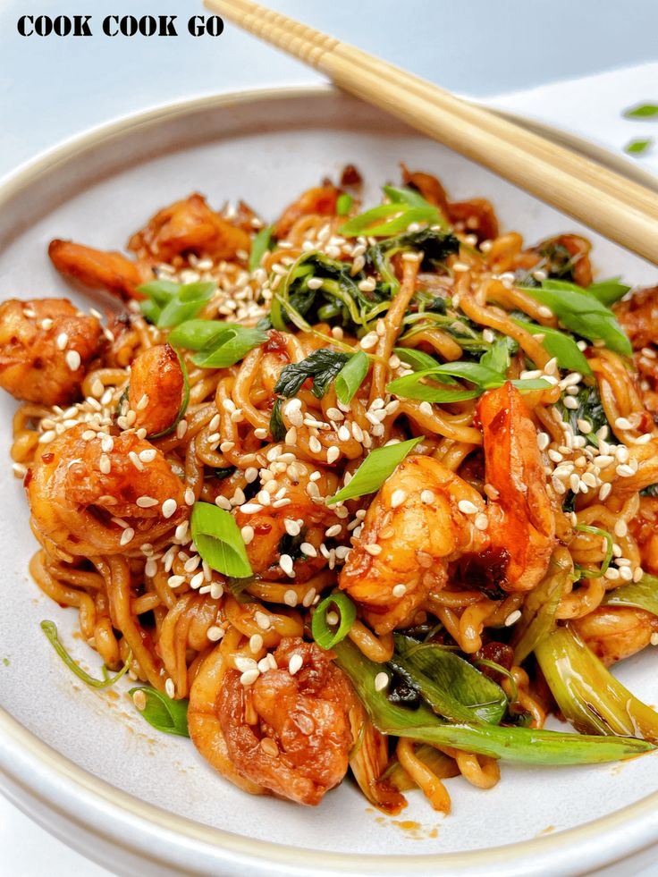 a white plate topped with noodles and shrimp next to chopsticks on a table