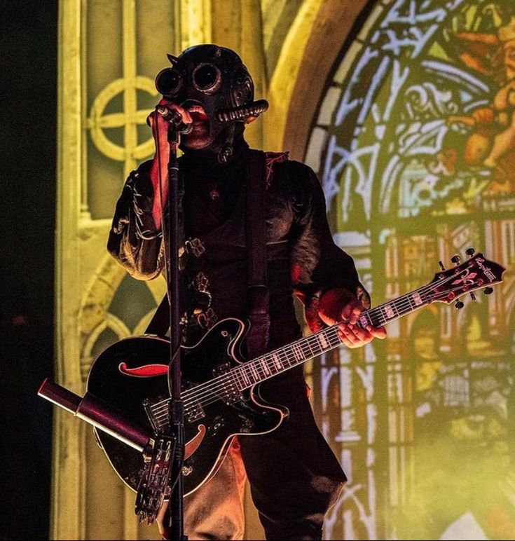 a man in gas mask holding a guitar on stage