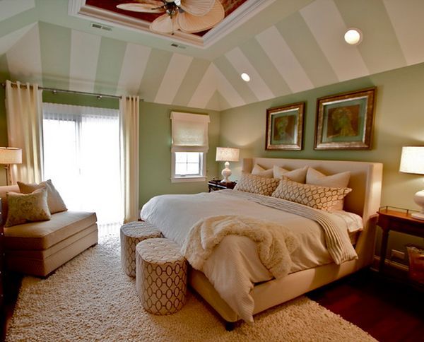 a bedroom with green walls and white carpeted flooring, large bed surrounded by beige furniture