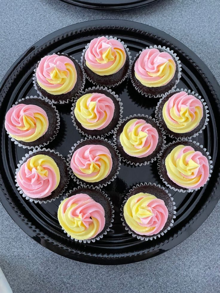 cupcakes with pink and yellow frosting on a black plate