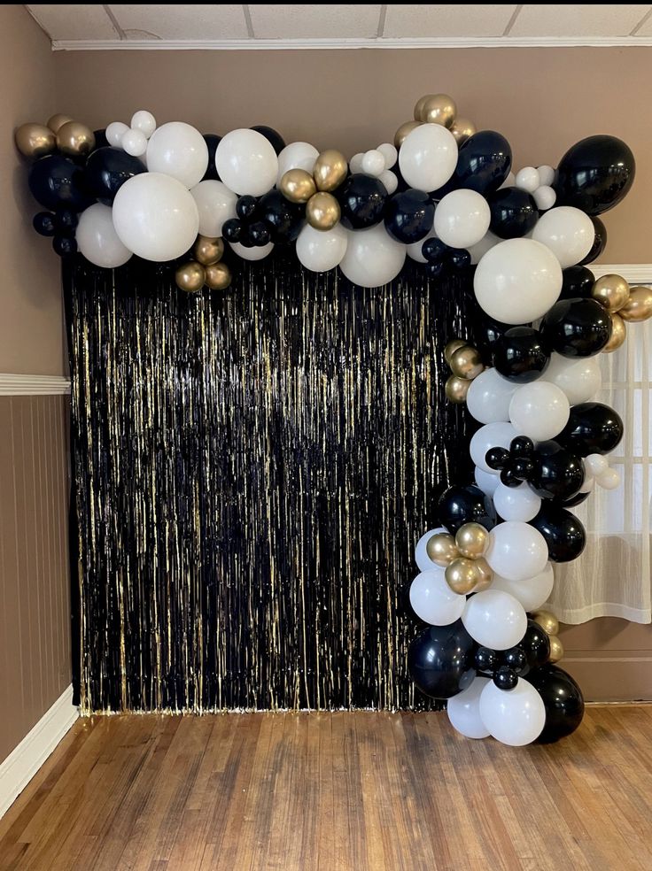 black and white balloons are hanging from the ceiling in front of a backdrop that has gold foil streamers on it