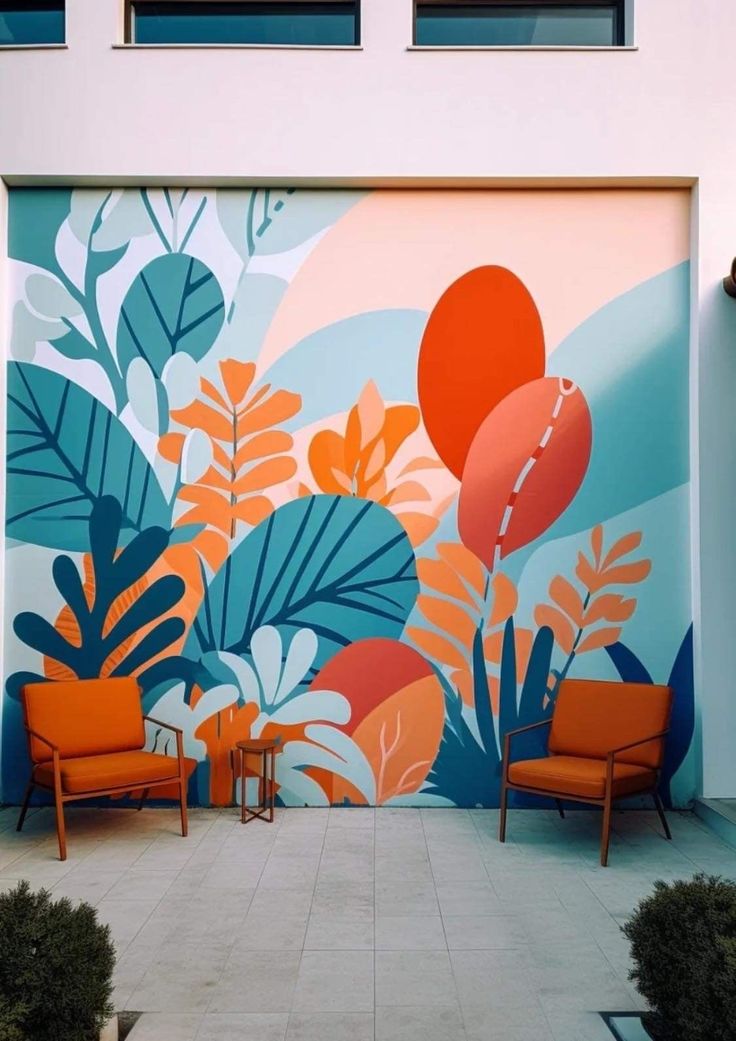 two orange chairs sitting in front of a colorful mural on the side of a building