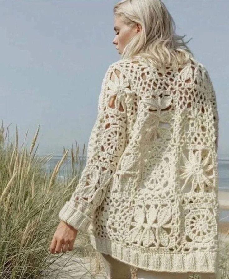 a woman standing on top of a sandy beach next to grass and sand dunes with the ocean in the background