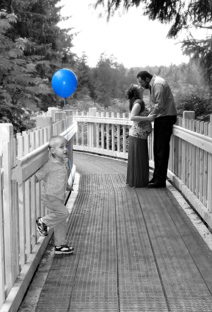 a black and white photo of a family on a bridge with a blue balloon in the air