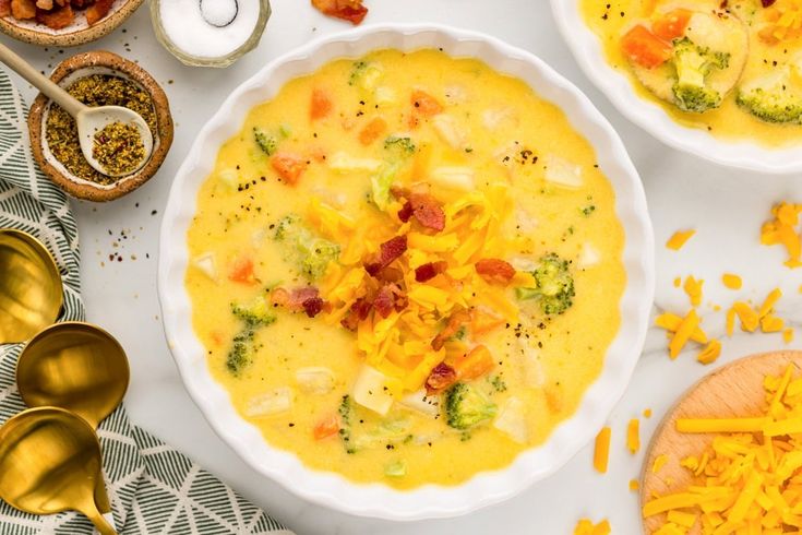 three bowls filled with different types of food on top of a white tablecloth next to gold spoons