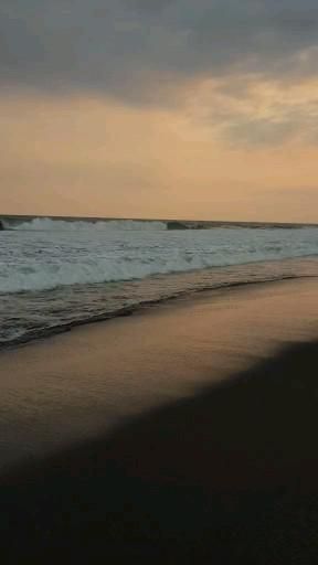 a person walking on the beach at sunset with their surfboard in hand and waves crashing into the shore