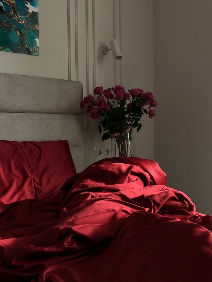 a vase filled with flowers sitting on top of a bed covered in red sheets and blankets