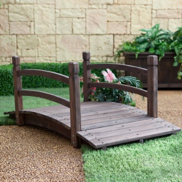 a miniature wooden bridge in the middle of some fake grass and potted plants behind it