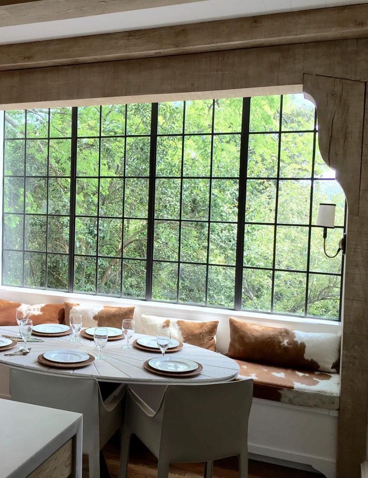 a dining room table with place settings in front of a large window overlooking the woods