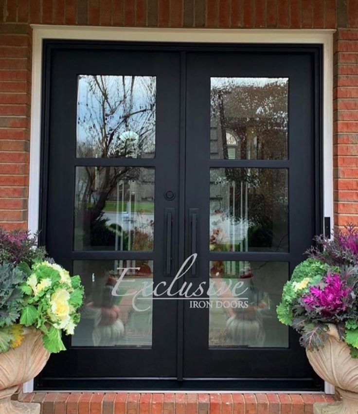 two large vases filled with flowers sitting in front of a black double glass door