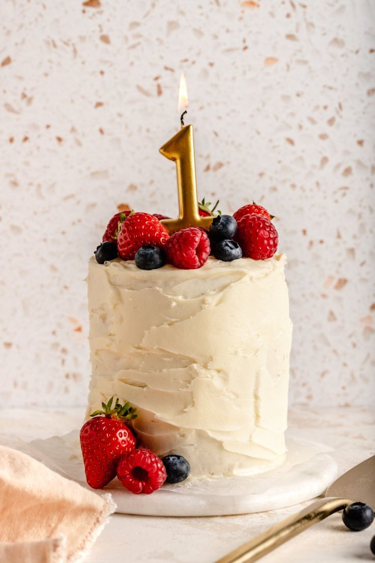 a white cake topped with berries and a gold number one candle on top of it