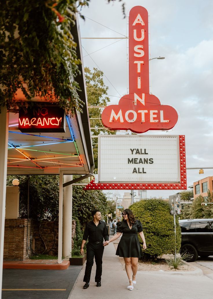 a man and woman walking down the street in front of a neon sign that says austin motel