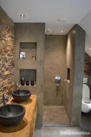 two black bowls are on the counter in this modern bathroom with stone walls and floor