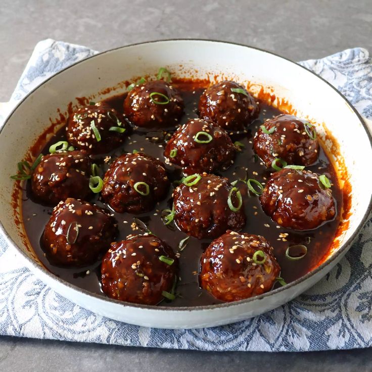 meatballs with sauce and green onions in a white bowl on a blue napkin next to a fork