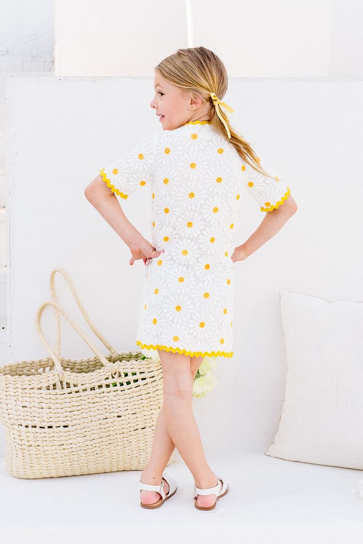 The Mini Delilah Dress will have you feeling like a dainty daisy in no time. With a playful white and yellow crocheted print, this knee-length dress features a V-neckline, contrasting trim, and functional front buttons adorned with pearls and rhinestones. Plus, the fully lined non-stretch fabric ensures both style and comfort. White Crochet Trim Dress For Vacation, Yellow Short Sleeve Dress With Lace Trim, Yellow Lace Trim Short Sleeve Dress, White Daisy Print Dress For Vacation, Spring Mini Dress With Crochet Trim, White Daisy Print Summer Dress, White Summer Dress With Daisy Print, Spring V-neck Dress With Crochet Trim, Spring Cotton Crochet Dress With V-neck