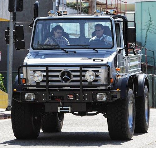 a mercedes benz truck driving down the street with two men sitting in the driver's seat