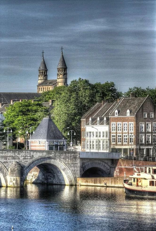 an old bridge over a river with boats on it and some buildings in the background