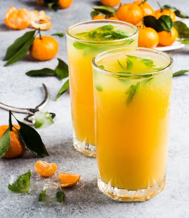 two glasses filled with orange juice and garnished with green leaves on the rim