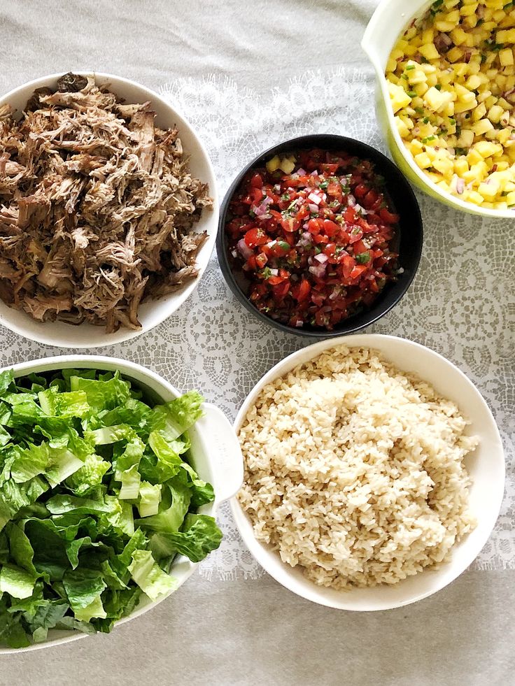 four bowls filled with different types of food on top of a white table covered in cloth