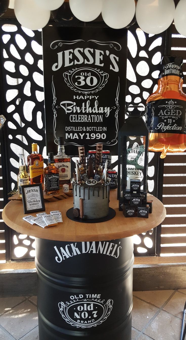 a birthday cake on top of a barrel with liquor bottles around it and balloons in the background