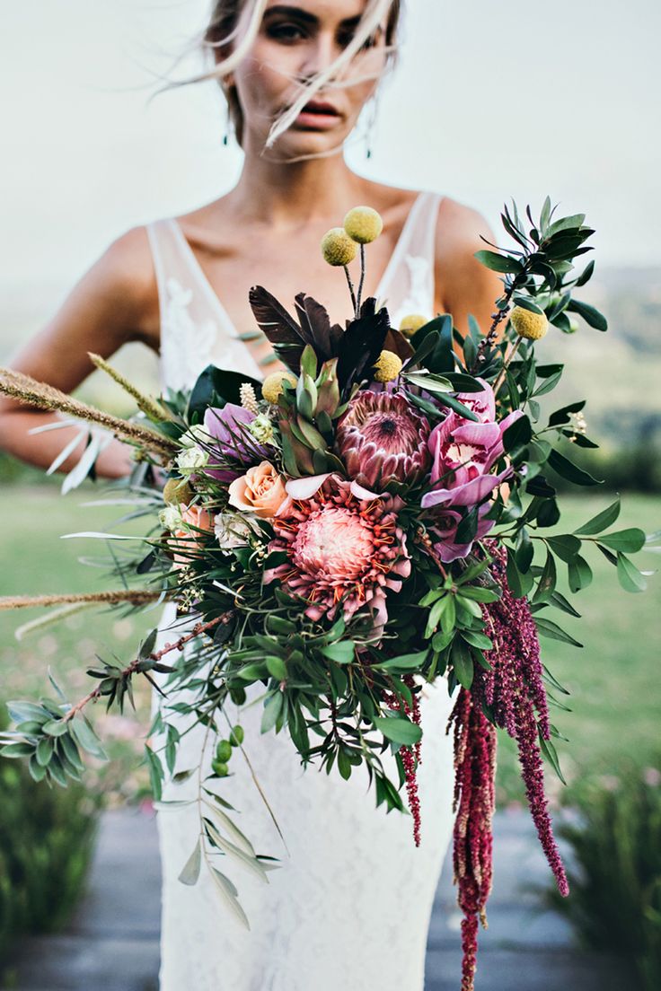 a woman holding a bouquet of flowers and greenery in front of her face,