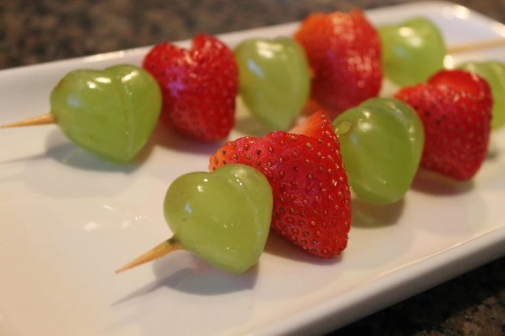 green and red strawberries are arranged on a white plate with toothpicks in the shape of hearts