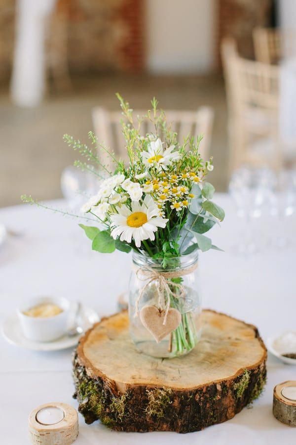 a vase filled with white flowers sitting on top of a wooden slice at a table