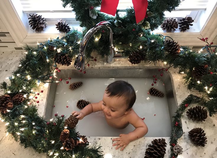 a baby in a bathtub surrounded by pine cones and christmas wreaths