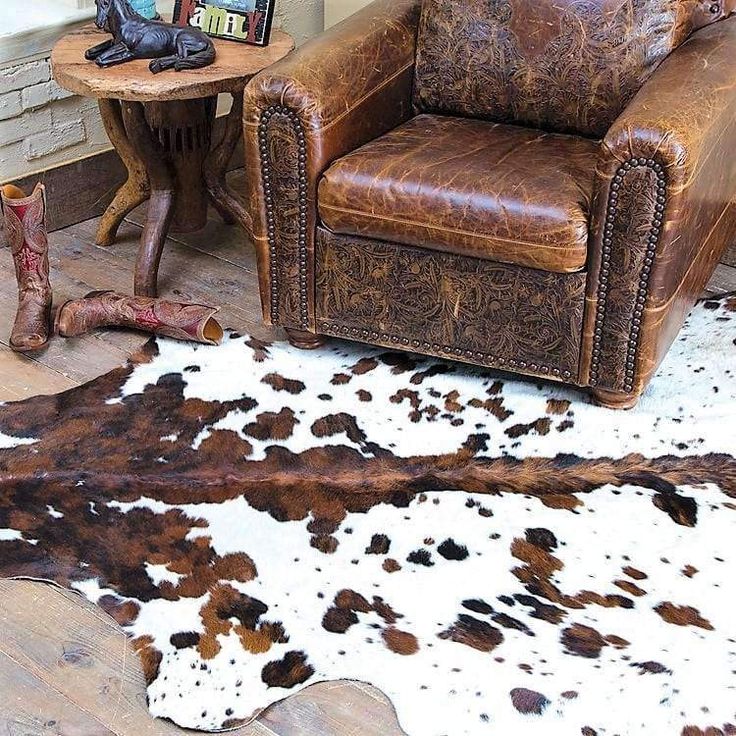 a cowhide rug is on the floor next to a leather chair and side table