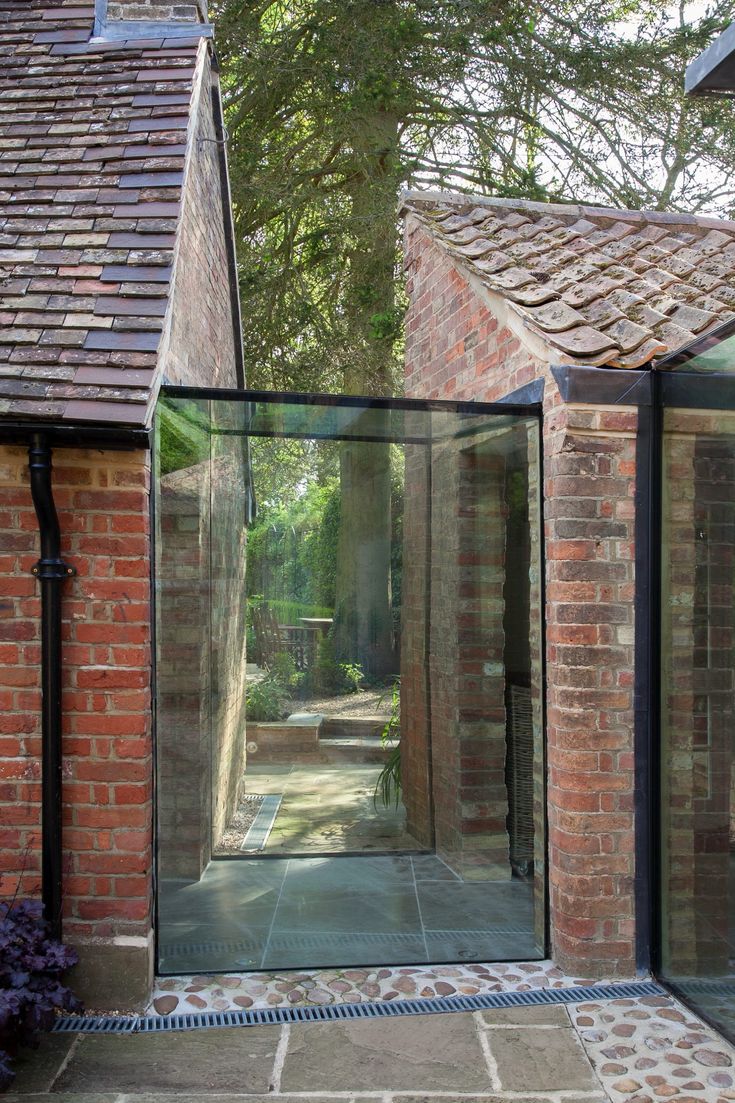 an open glass door leading to a brick building in the middle of a garden area