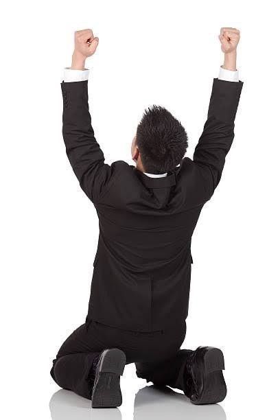 a man sitting on the ground with his arms up in triumph and fists raised above his head