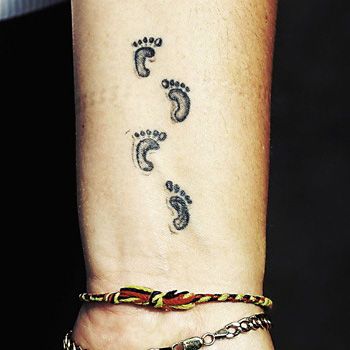 a woman's foot with three footprints tattooed on her left arm and two bracelets attached to the wrist