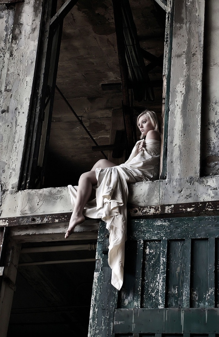 a woman sitting on top of a wooden window sill next to an old building