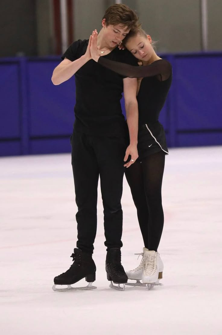 two people on ice skates in an indoor skating rink, one is hugging the other's head