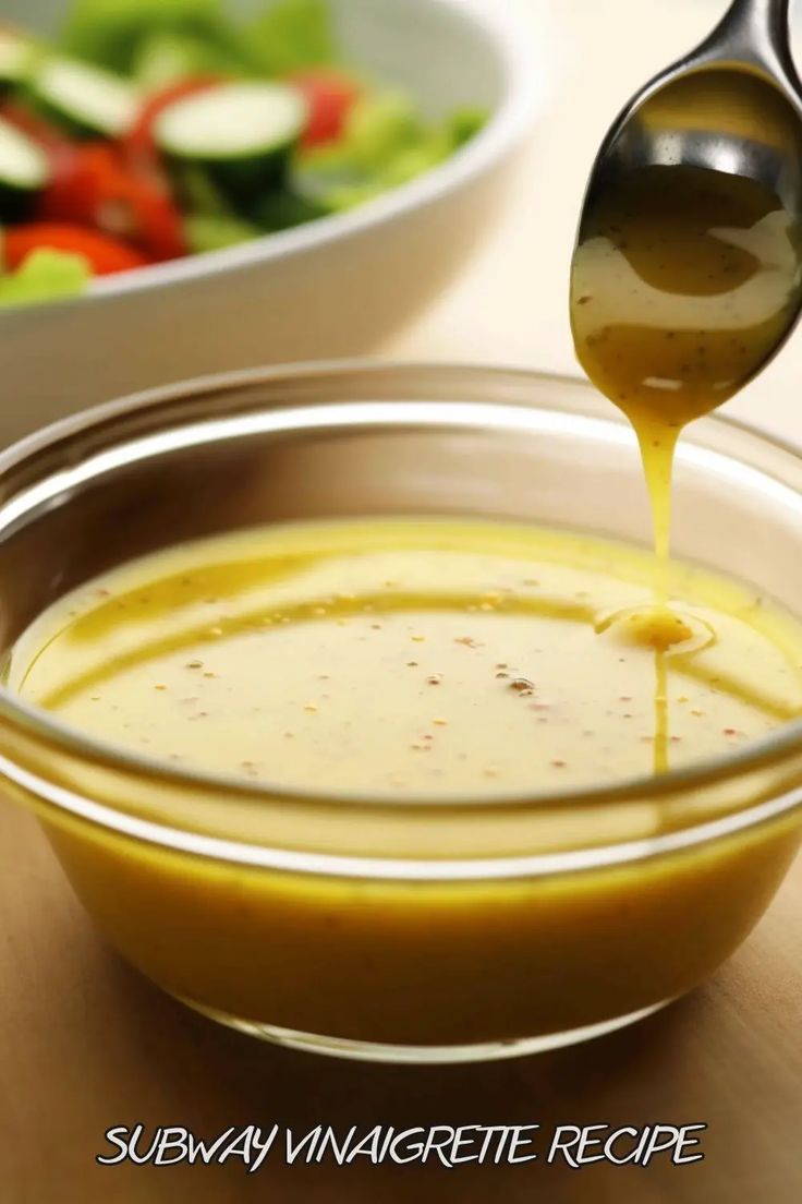 a spoon is pouring dressing into a bowl with salad in the background and another bowl behind it