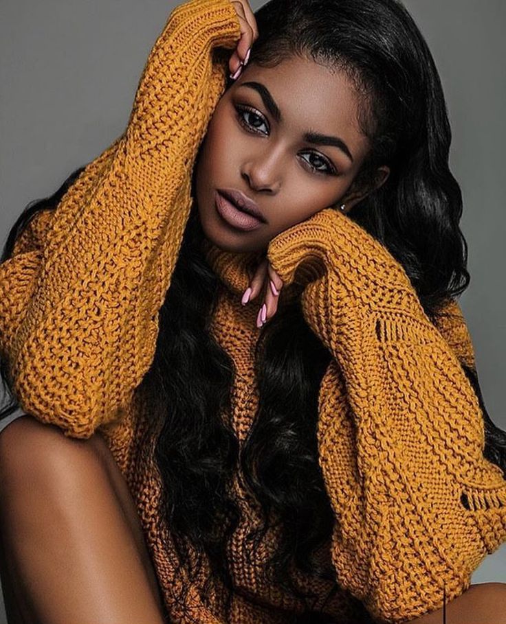 a woman with long black hair wearing a yellow sweater and holding her hands on her head