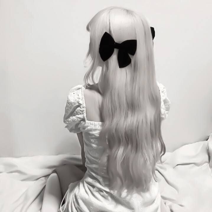 a woman with long white hair and black bow tie on her head sitting on a bed