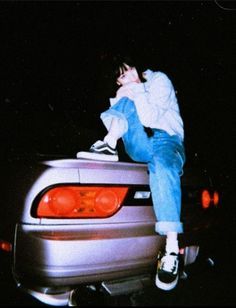 a young man sitting on the back of a silver car in front of a black background