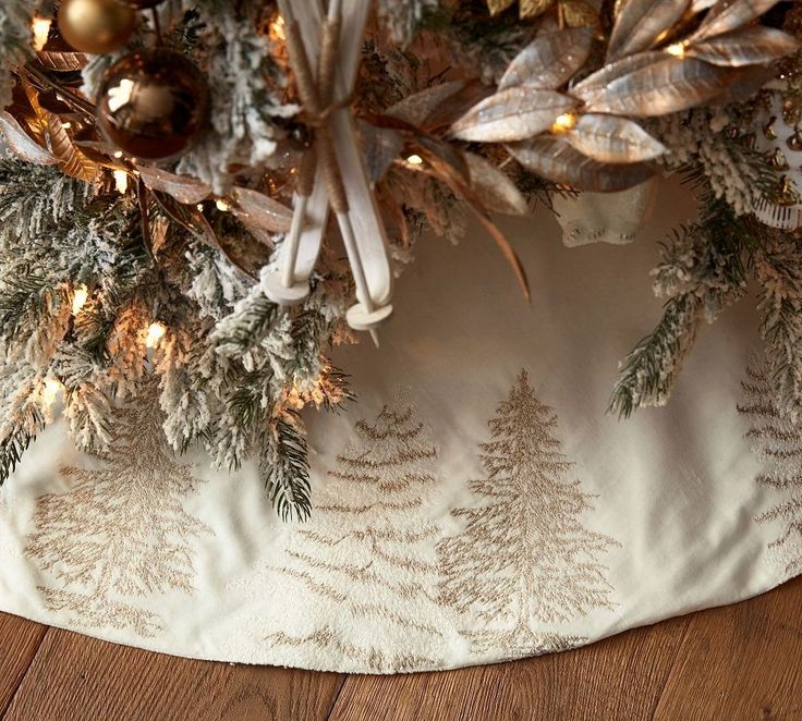 a christmas tree skirt with gold ornaments and pine trees on the bottom, along with white ribbon