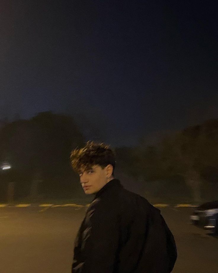 a young man riding a skateboard down a street next to a parking lot at night