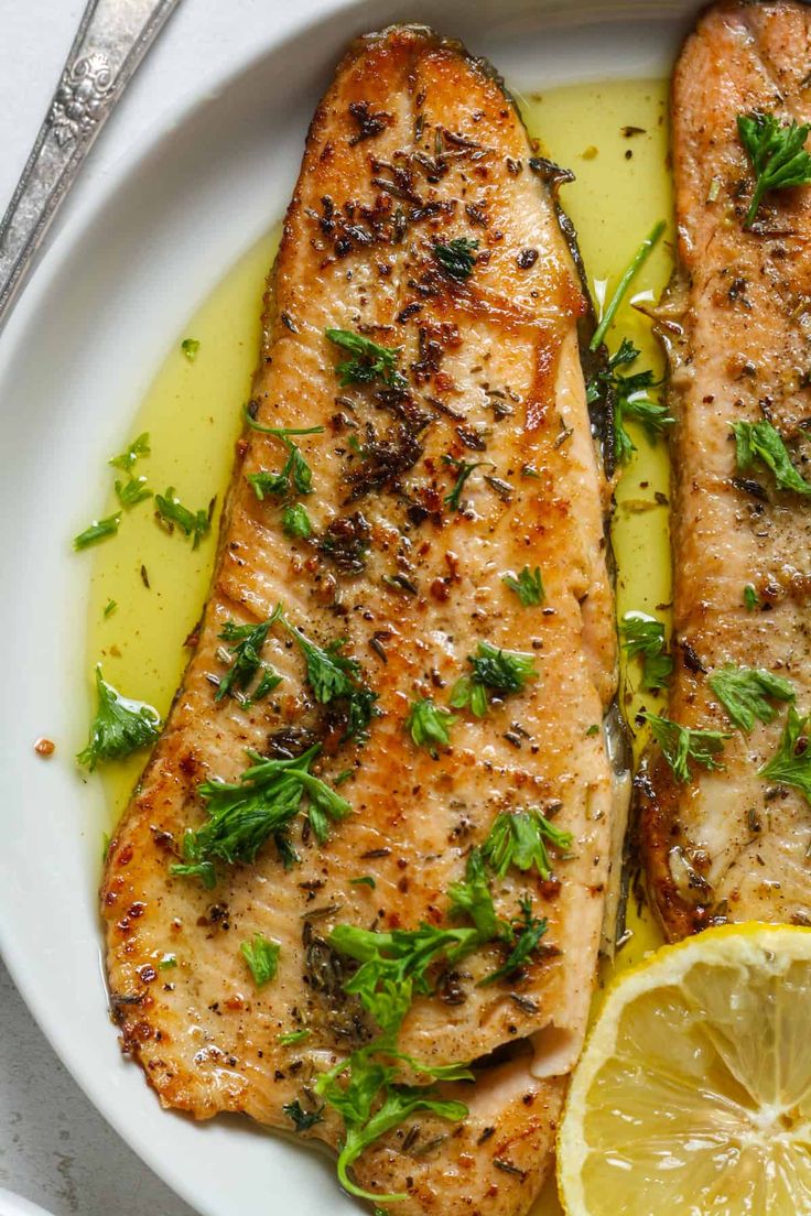 two fish fillets on a plate with lemon and parsley