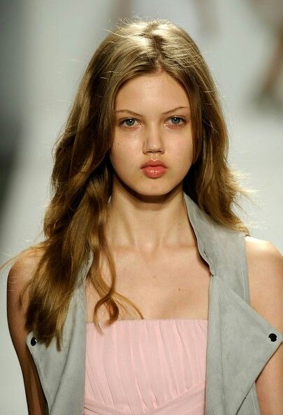 a model walks down the runway in a pink dress and gray jacket with long hair