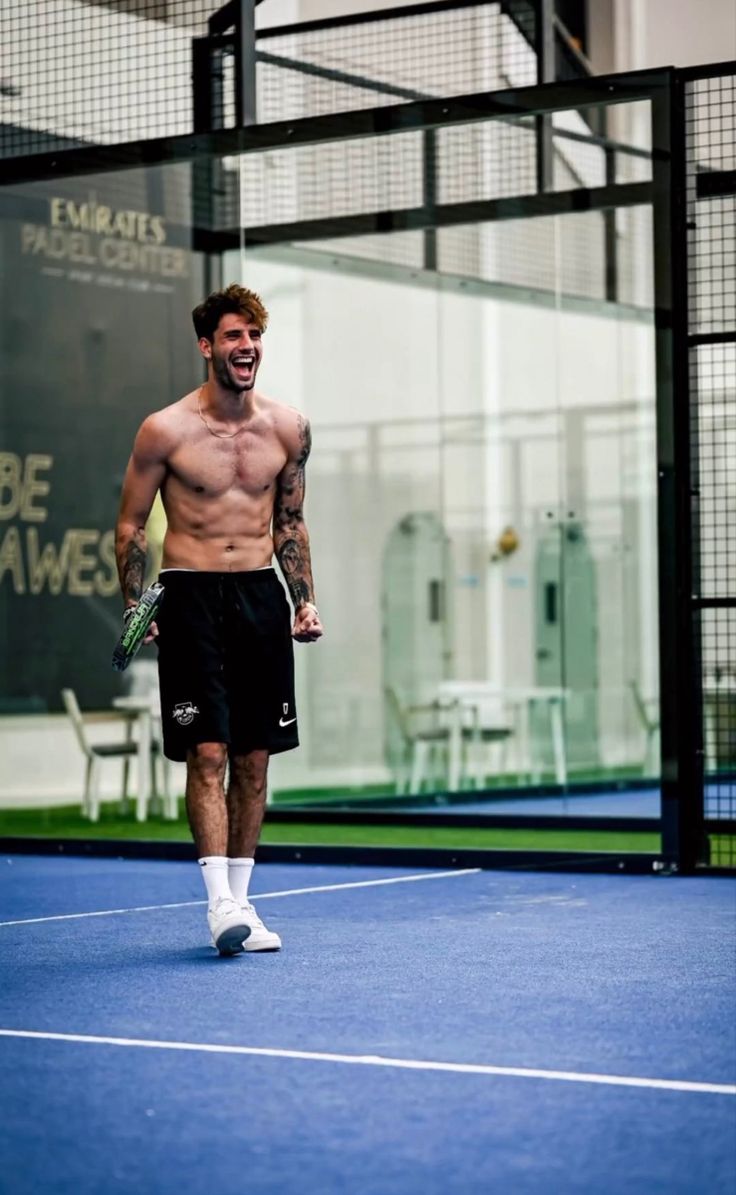 a shirtless male tennis player is walking on the court with his racquet