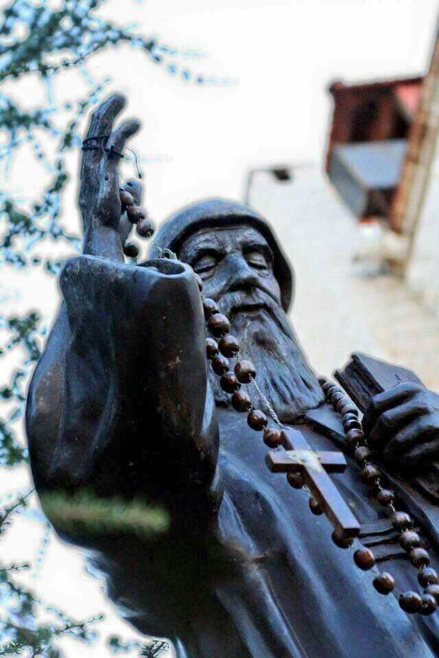 a statue of a man with beads on his head and hands in front of a building