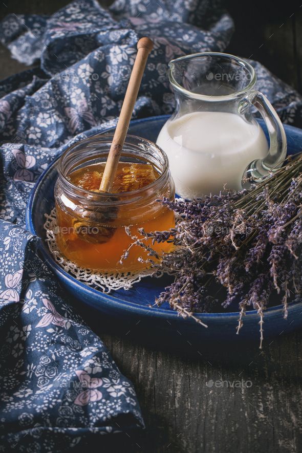 a blue plate topped with honey and lavenders next to a glass jar filled with milk