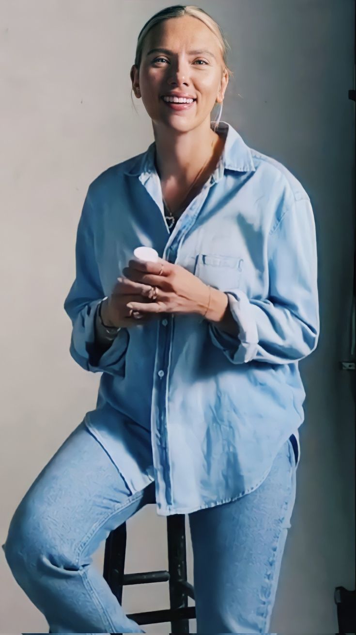 a woman sitting on top of a chair holding a remote control in her hand and smiling